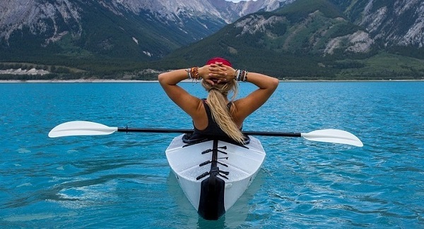 Frau im Kajak entspannt sich auf dem Wasser und blickt in die Ferne als Symbol für Wohlbefinden im Alltag durch Körpertherapie nach der Grinberg Methode.